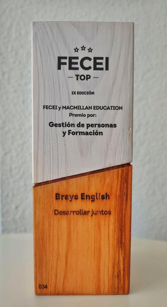 The prize we won at the event. It's a wooden cuboid with the top half painted white. It says FECEI TOP IX EDICIÓN FECEI Y MACMILLAN EDUCATION PREMIO POR:GESTIÓN DE PERSONAS Y FORMACIÓN. At the bottom, unpainted, it says: BRAYS ENGLISH DESARROLLAR JUNTOS